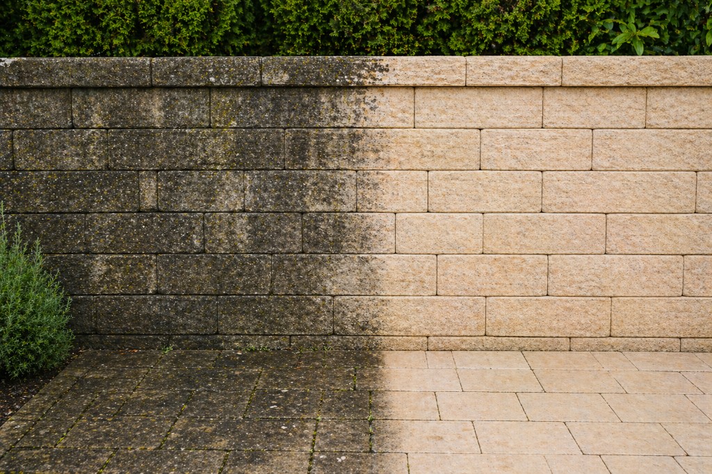 Mauerreinigung Vorher/Nachher: Steinmauer und Pflaster links mit Algen und Moos, rechts professionell gereinigt, hellbeige Oberfläche